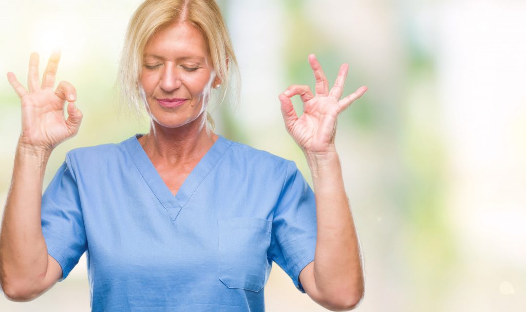 Middle age blonde woman wearing doctor nurse uniform over isolated background relax and smiling with eyes closed doing meditation gesture with fingers. Yoga concept.