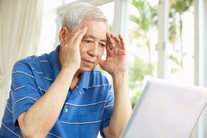 Senior Chinese Man Sitting At Desk Using Laptop In Home - Telehealth